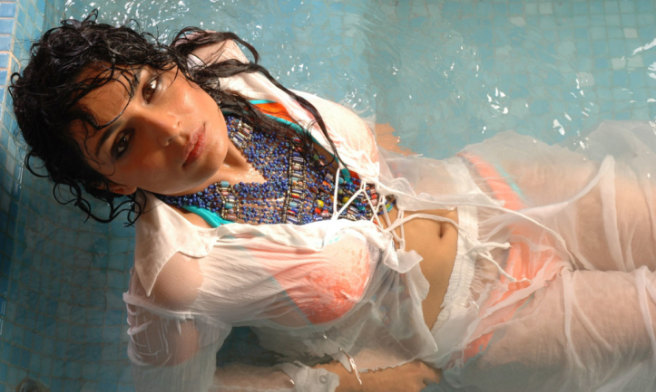 Meera (Irtiza Rubab) relaxes in the swimming pool wearing a teal and orange bikini under sheer see-thru whites clothes. Her neckline is adorned with a traditional Sindhi necklace.
